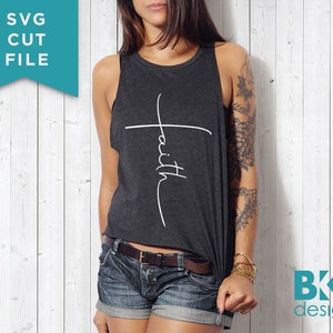 May include: A woman wearing a dark gray tank top with the word "faith" written vertically on a white cross. The tank top is cropped and the woman is wearing denim shorts.