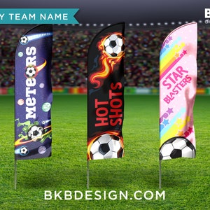 May include: Three soccer team flags with different designs. The first flag is blue with a space theme and the words "Meteors" in white. The second flag is black with a fire design and the words "Hot Shots" in red. The third flag is pink with a rainbow design and the words "Star Blasters" in white.