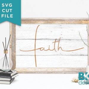 May include: A white wooden sign with a rustic wood frame, featuring the word "faith" written in a cursive script in copper foil. The sign is sitting on a white surface with decorative items.