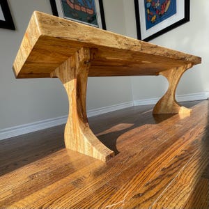 Peut inclure: Une table basse en bois avec une finition en bois naturel et un piétement unique et incurvé. La table est en bois massif et a un style rustique et champêtre.