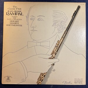 May include: Vintage vinyl record album cover featuring a line drawing of a man with a bow tie, holding a flute. The album title is "The Classic Flute Jean-Pierre Rampal." The cover has the RCA Red Seal logo and the Erato Collection logo.