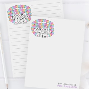 May include: Two white lined notepads with a colorful beaded bracelet design that says "In My Teacher Era". The bottom notepad has the text "from the desk of MRS. ANDERSON" and the text "pastel > teacher era".