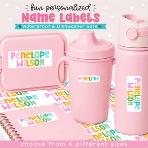 May include: A set of light pink items including a lunch box, a sippy cup, and a water bottle, each featuring white rectangular name labels with the text Penelope Wilson in colorful, rounded letters. The labels are waterproof and dishwasher safe.