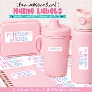 May include: A set of light pink items including a lunch box, a sippy cup, and a water bottle, each featuring white rectangular name labels with the text Penelope Wilson in pastel purple and blue letters. The labels are waterproof and dishwasher safe.