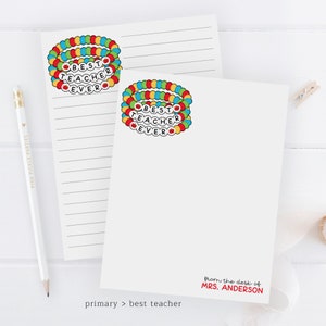 Puede incluir: Dos blocs de notas blancos con l&iacute;neas con un dise&ntilde;o de pulsera de cuentas de colores que dice "Mejor Maestro de Todos los Tiempos". El bloc de notas de abajo tiene el texto "desde el escritorio de la Sra. ANDERSON" en rojo.