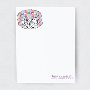 Puede incluir: Una tarjeta blanca con el texto "In My Teacher Era" en letras rosa, azul y amarillo. Las letras est&aacute;n rodeadas por una pila de tres pulseras de cuentas de colores. El texto "from the desk of MRS. ANDERSON" est&aacute; en la parte inferior de la tarjeta.