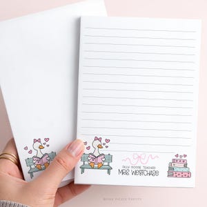 May include: A white notepad and envelope set. The notepad has lined pages and a cartoon goose reading a book on a bench. The text reads "Silly Goose Teacher Mrs. Westchase". Pink hearts and books are also featured.