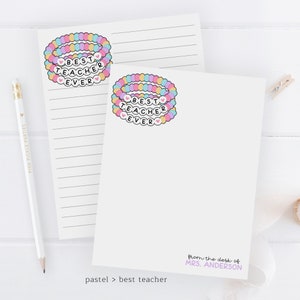 Puede incluir: Dos tarjetas de notas en blanco con l&iacute;neas con un dise&ntilde;o de pulsera de cuentas de arco&iacute;ris pastel que dice "Mejor Maestro de Todos los Tiempos" en cada tarjeta. El texto "desde el escritorio de la Sra. ANDERSON" est&aacute; en la parte inferior de una tarjeta. El texto "pastel > mejor maestro" est&aacute; en la parte inferior de la otra tarjeta.