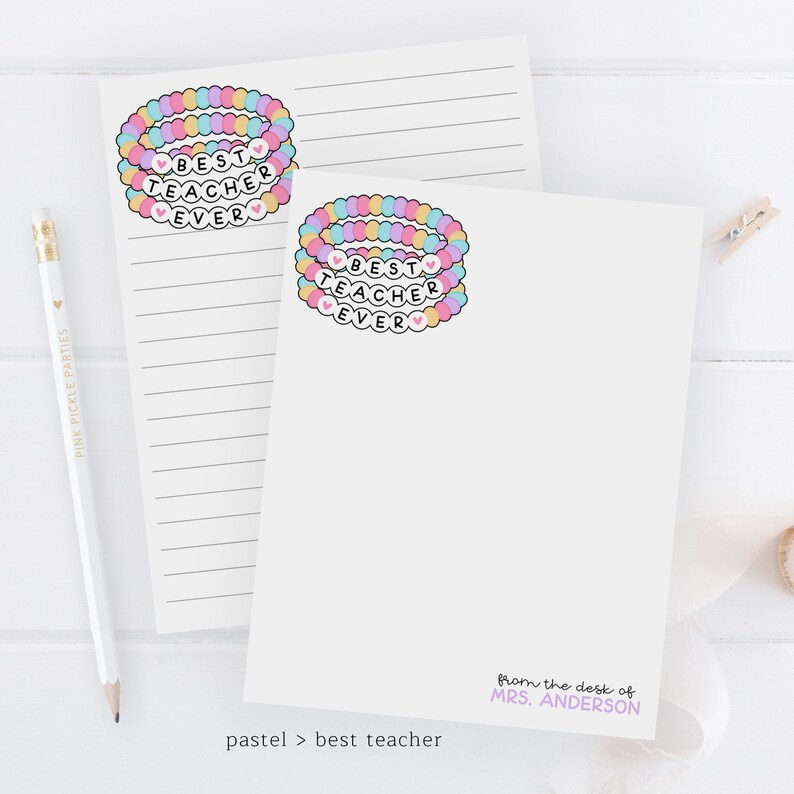 Puede incluir: Dos tarjetas de notas en blanco con l&iacute;neas con un dise&ntilde;o de pulsera de cuentas de arco&iacute;ris pastel que dice "Mejor Maestro de Todos los Tiempos" en cada tarjeta. El texto "desde el escritorio de la Sra. ANDERSON" est&aacute; en la parte inferior de una tarjeta. El texto "pastel > mejor maestro" est&aacute; en la parte inferior de la otra tarjeta.