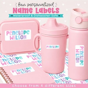 May include: A collection of pink items including a lunch box, a sippy cup, and a water bottle, each featuring white rectangular name labels with the text Penelope Wilson in teal and purple. The labels are also displayed on a sheet below.