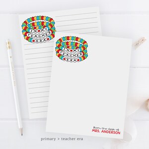 Puede incluir: Dos blocs de notas blancos con papel rayado. Cada bloc de notas tiene una pulsera colorida con las palabras "I love my teacher era" en ella. El bloc de notas inferior tiene el texto "from the desk of MRS. ANDERSON" impreso en &eacute;l.