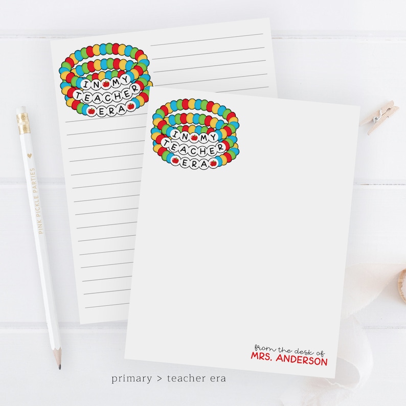 Puede incluir: Dos blocs de notas blancos con papel rayado. Cada bloc de notas tiene una pulsera colorida con las palabras "I love my teacher era" en ella. El bloc de notas inferior tiene el texto "from the desk of MRS. ANDERSON" impreso en &eacute;l.