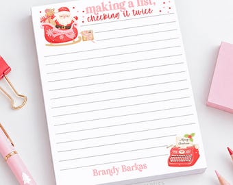 May include: A white lined notepad featuring the text "making a list, checking it twice" in pink and red. The top left shows Santa in a red sleigh with gifts. The bottom right features a red typewriter with a "Merry Christmas" note.