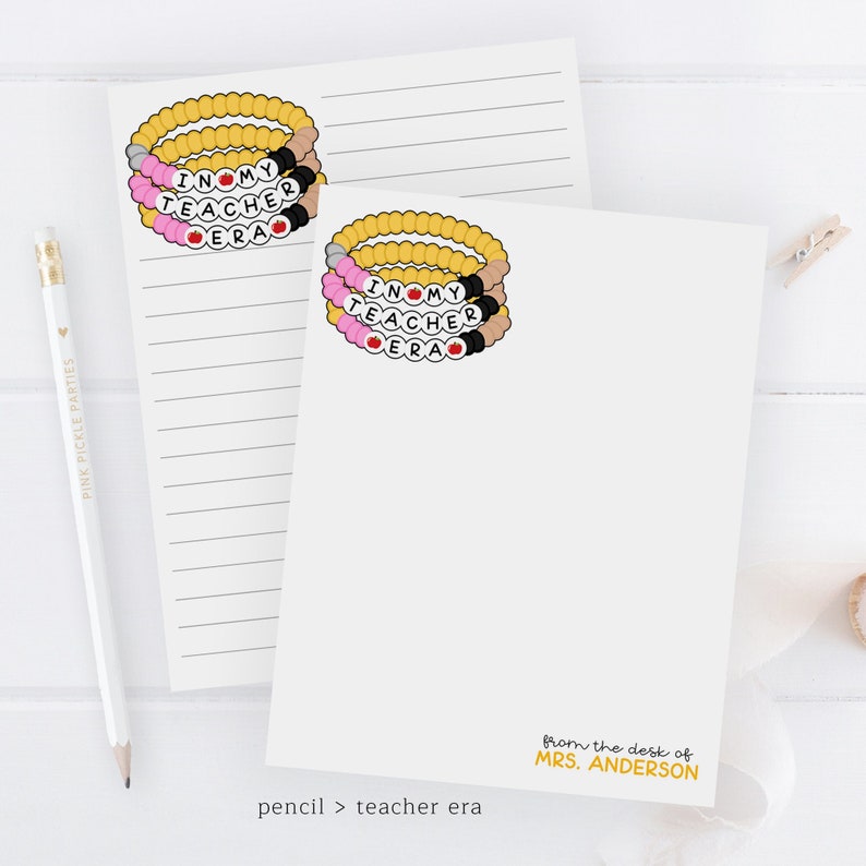 Puede incluir: Dos blocs de notas blancos con papel rayado. El bloc de notas superior tiene una pila de pulseras de cuentas de colores con las palabras "Me encanta mi &eacute;poca de maestra" en ellas. El bloc de notas inferior tiene las mismas pulseras y el texto "desde el escritorio de la Sra. ANDERSON".
