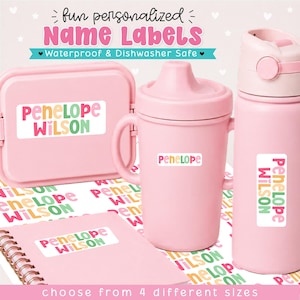 May include: A collection of light pink items including a snack container, a sippy cup, a water bottle, and a spiral notebook, all featuring personalized white rectangular name labels with the text Penelope Wilson in colorful, rounded lettering.