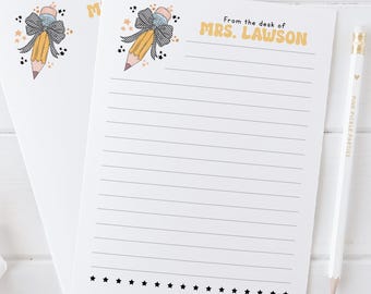 May include: A white lined notepad with a yellow pencil with a blue bow and black stars. The notepad has the text "From the desk of MRS. LAWSON" at the top.