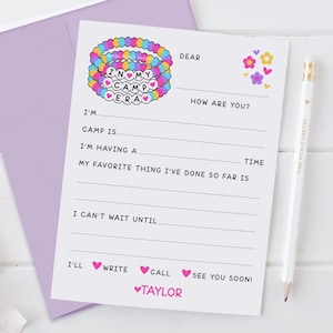 May include: A white fill-in-the-blank postcard with a purple envelope. The postcard features a colorful bracelet graphic with the words "IN MY CAMP ERA". The text includes prompts like "Dear", "How are you?", and "I'm having a". A white pencil is on the right.