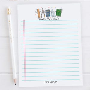 May include: A white notepad with horizontal blue lines and two vertical pink margin lines. The top features a cartoon illustration of a ruler, compass, calculator, triangle, and book with the text Math Teacher. The bottom displays the name Mrs. Carter.