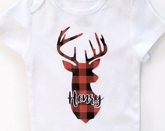 Op de afbeelding: Witte baby romper met een rood en zwart geruit hert silhouet en de naam "Henry" eronder.