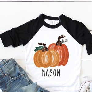 Pode incluir: Uma camiseta de beisebol branca e preta com um desenho de tr&ecirc;s ab&oacute;boras laranja e o nome "MASON" impresso na frente. A camiseta &eacute; combinada com jeans azul e t&ecirc;nis brancos.