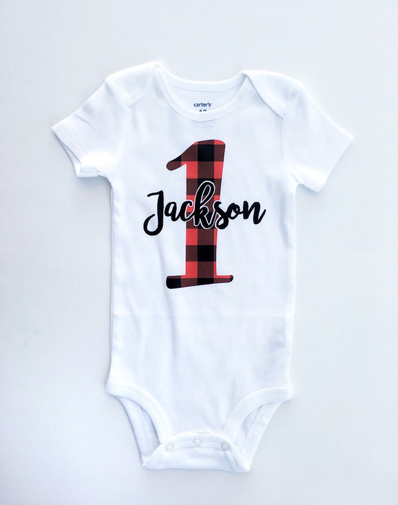 May include: White onesie with a red and black buffalo plaid number one and the name Jackson in black script.