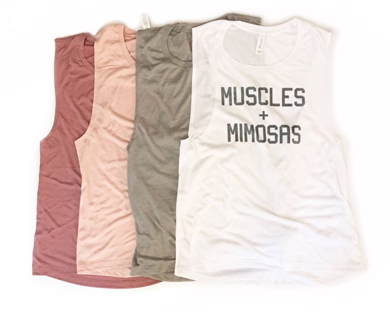 Puede incluir: Cuatro camisetas sin mangas de diferentes colores. La camiseta blanca tiene el texto "MUSCLES + MIMOSAS" impreso.