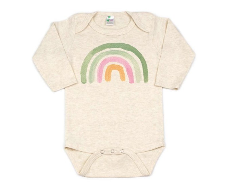 Op de afbeelding: Een beige baby-romper met lange mouwen en een regenboogprint. De regenboog is geschilderd in tinten groen, roze en oranje.