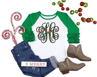 Op de afbeelding: Wit langarm shirt met groene raglanmouwen en een rood-groen geruit monogram. Het shirt heeft ruches op de mouwen. Het shirt wordt gecombineerd met een blauwe jeans en bruine enkellaarsjes. De tekst "BE MERRY" staat op een wit bord.