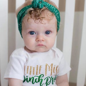 Puede incluir: Una ni&ntilde;a peque&ntilde;a con un body blanco con texto de purpurina dorada que dice "Little Miss Pinch Proof" y una diadema verde con texto blanco.