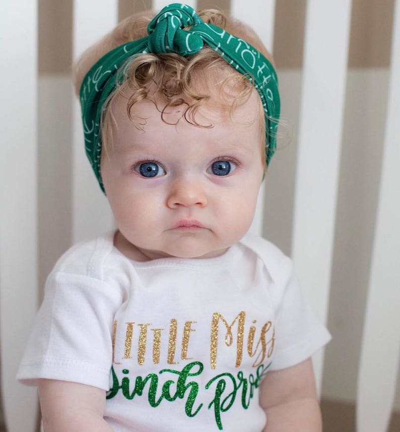 Puede incluir: Una ni&ntilde;a peque&ntilde;a con un body blanco con texto de purpurina dorada que dice "Little Miss Pinch Proof" y una diadema verde con texto blanco.