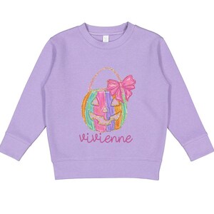 Puede incluir: Una sudadera de color lavanda con un dise&ntilde;o de calabaza colorida y el nombre "vivienne" impreso en la parte delantera.
