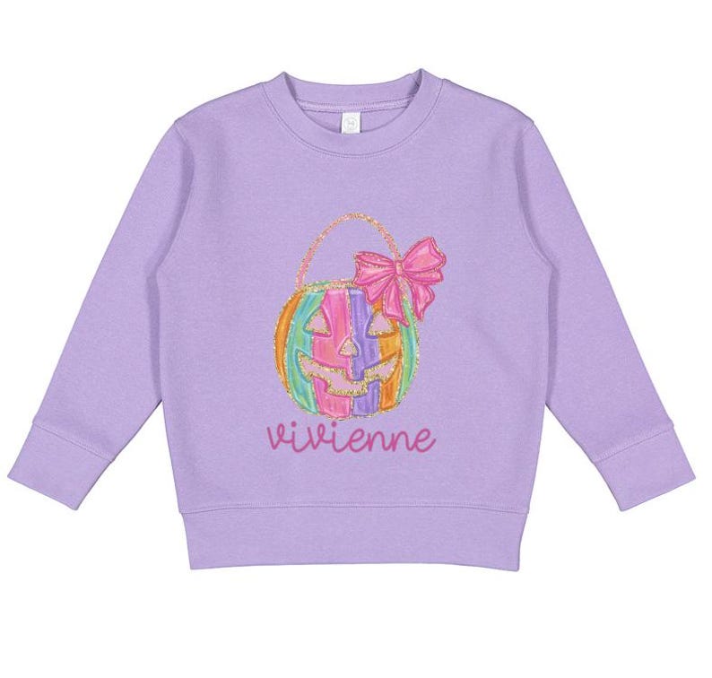 Puede incluir: Una sudadera de color lavanda con un dise&ntilde;o de calabaza colorida y el nombre "vivienne" impreso en la parte delantera.