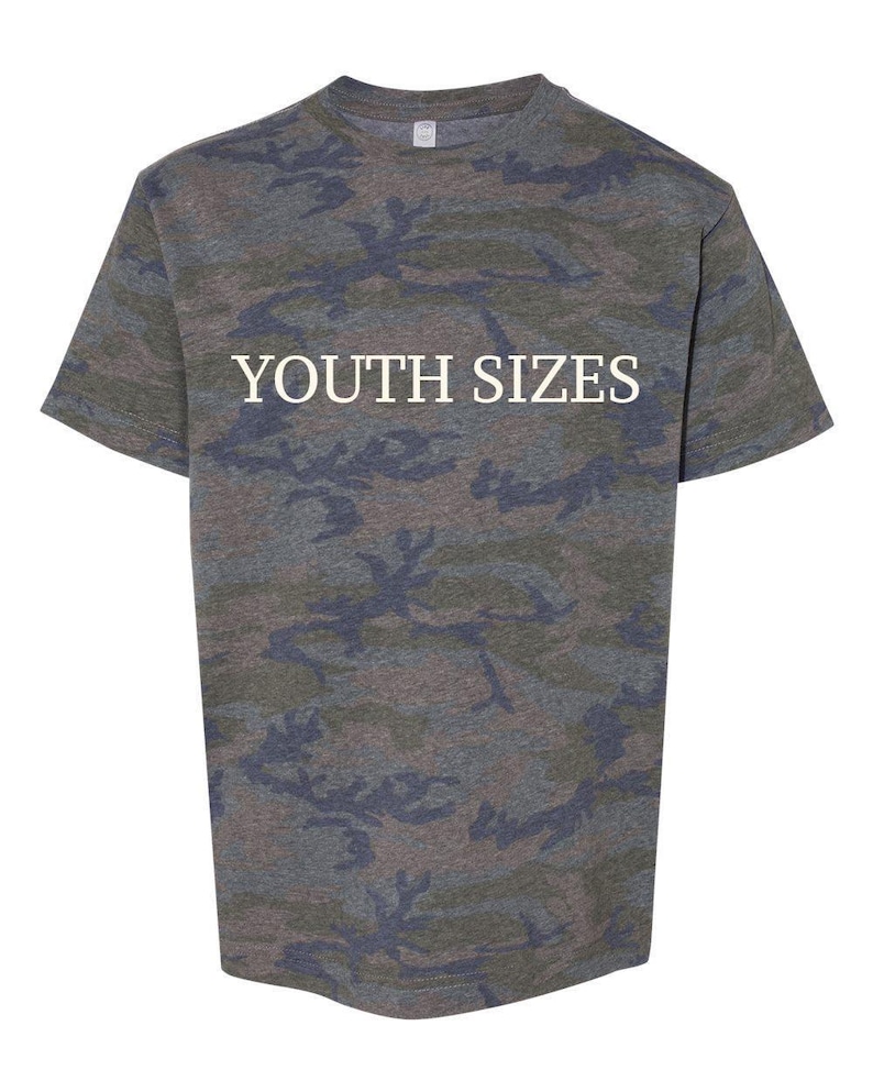 May include: A short-sleeved t-shirt featuring a camouflage pattern in shades of green, brown, and dark gray. The text YOUTH SIZES is printed in white capital letters across the center of the chest area on the front of the garment.