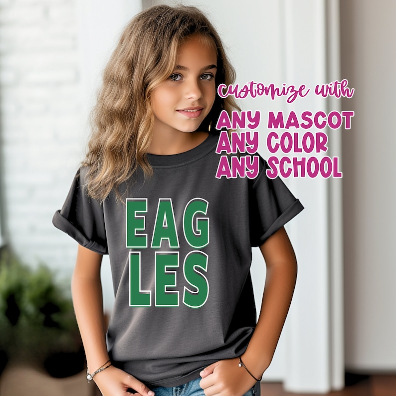 K&ouml;nnte beinhalten: Ein graues T-Shirt mit dem Wort "EAGLES" in gr&uuml;nen Buchstaben. Der Text "mit JEDEM MASKOTTCHEN JEDER FARBE JEDE SCHULE anpassen" ist in rosa Buchstaben.