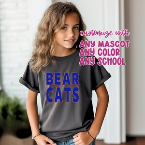 K&ouml;nnte beinhalten: Ein graues T-Shirt mit den Worten "BEAR CATS" in blauen und orangen Buchstaben. Der Text "mit JEDEM MASKOTTCHEN JEDER FARBE JEDE SCHULE anpassen" ist in rosa Buchstaben.