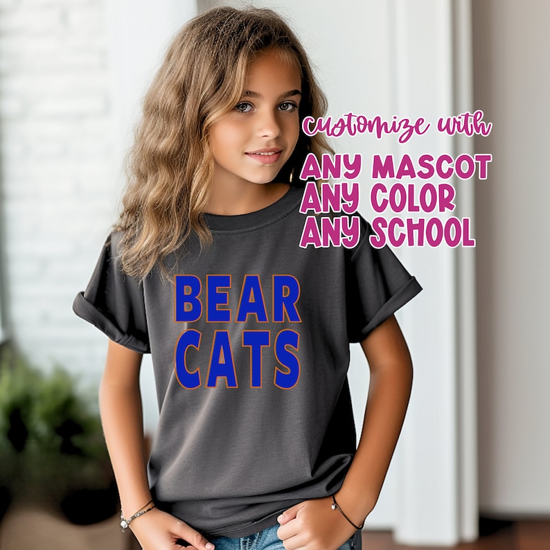 K&ouml;nnte beinhalten: Ein graues T-Shirt mit den Worten "BEAR CATS" in blauen und orangen Buchstaben. Der Text "mit JEDEM MASKOTTCHEN JEDER FARBE JEDE SCHULE anpassen" ist in rosa Buchstaben.