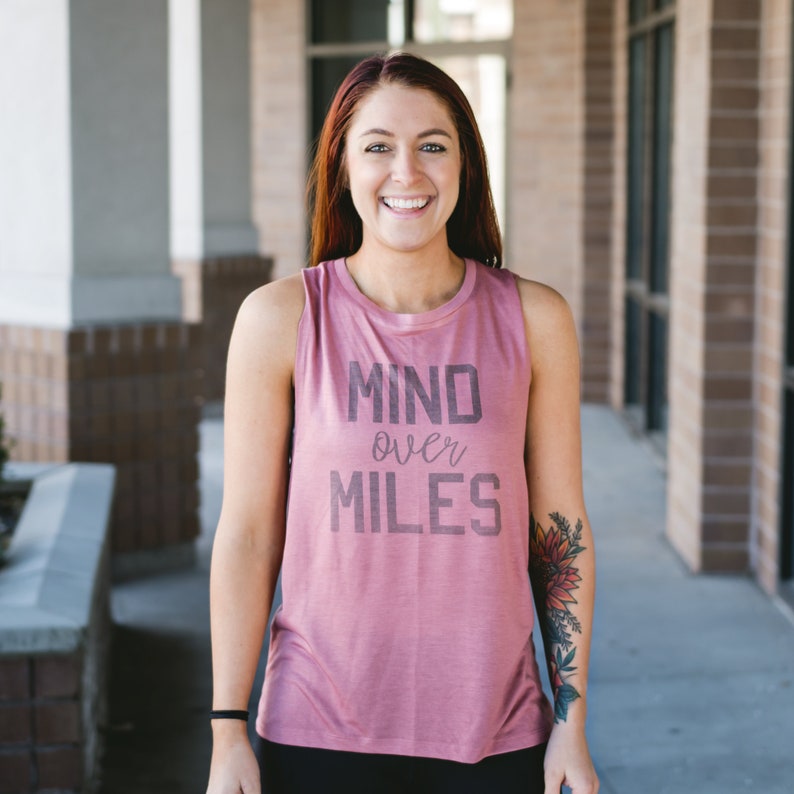 Puede incluir: Una mujer con una camiseta de tirantes rosa con el texto "MIND over MILES" impreso en la parte delantera. Est&aacute; sonriendo y mirando a la c&aacute;mara.