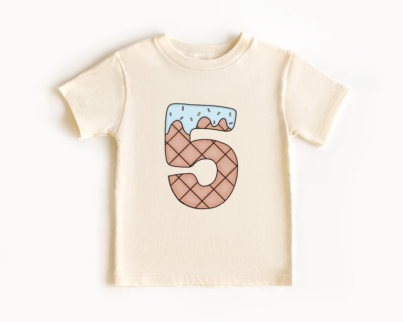 May include: A cream colored t-shirt with a cartoon ice cream cone shaped like the number 5. The ice cream is blue with pink sprinkles.