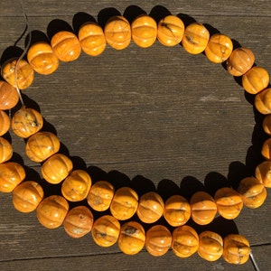 May include: A strand of orange pumpkin-shaped beads. The beads are a warm, golden-orange color with carved ridges, strung on a thin, clear string. The beads are arranged in a circular shape.