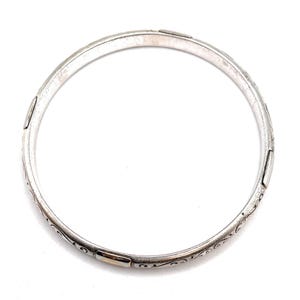 May include: A silver bangle bracelet with an intricate floral design and gold accents.