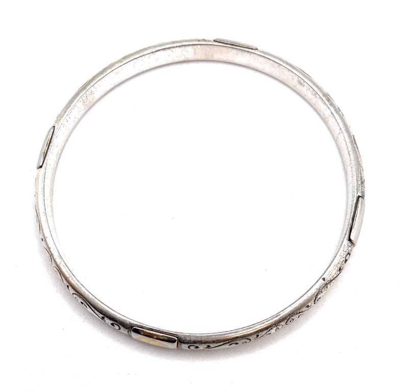 May include: A silver bangle bracelet with an intricate floral design and gold accents.