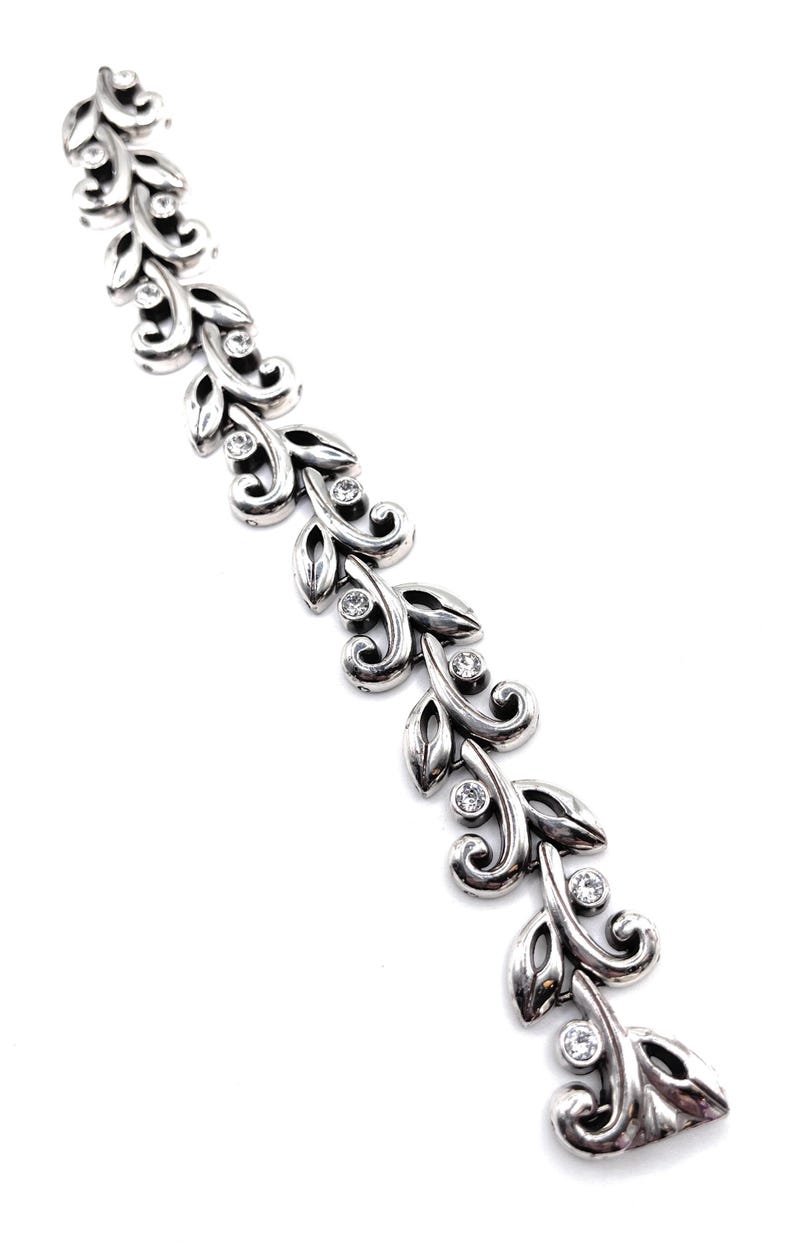 Puede incluir: Una pulsera plateada con un dise&ntilde;o de hojas y gemas transparentes. La pulsera presenta una serie de hojas estilizadas conectadas por eslabones curvos, con una gema redonda en el centro de cada hoja. La pulsera se muestra sobre un fondo blanco.
