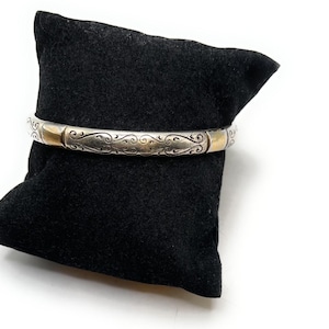 May include: A silver bangle bracelet with a gold accent and an intricate floral design.