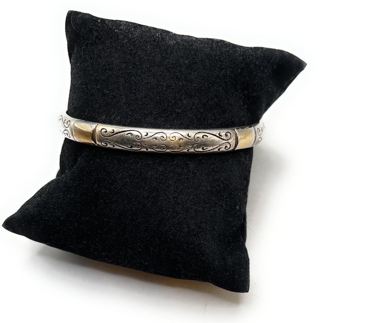 May include: A silver bangle bracelet with a gold accent and an intricate floral design.