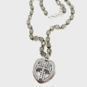 Peut inclure: Un collier argent&eacute; avec un pendentif en forme de c&oelig;ur et un motif de croix. Le pendentif est orn&eacute; de cristaux transparents. Le collier a une cha&icirc;ne perl&eacute;e avec des perles facett&eacute;es vert olive.