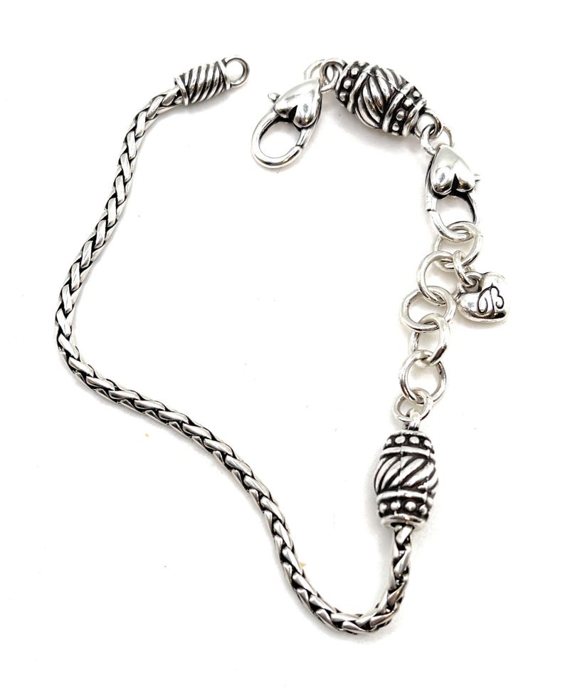 May include: A silver chain bracelet with a braided chain, a heart-shaped clasp, and two decorative beads.