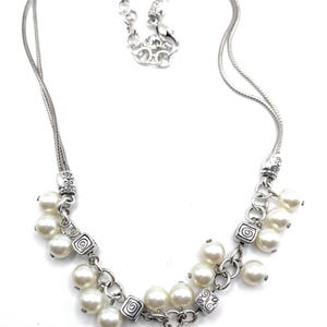 May include: Silver-toned necklace with multiple strands and a cluster of faux pearls. The necklace features decorative square links with a spiral design and a lobster clasp closure. The necklace is approximately 16 inches long.