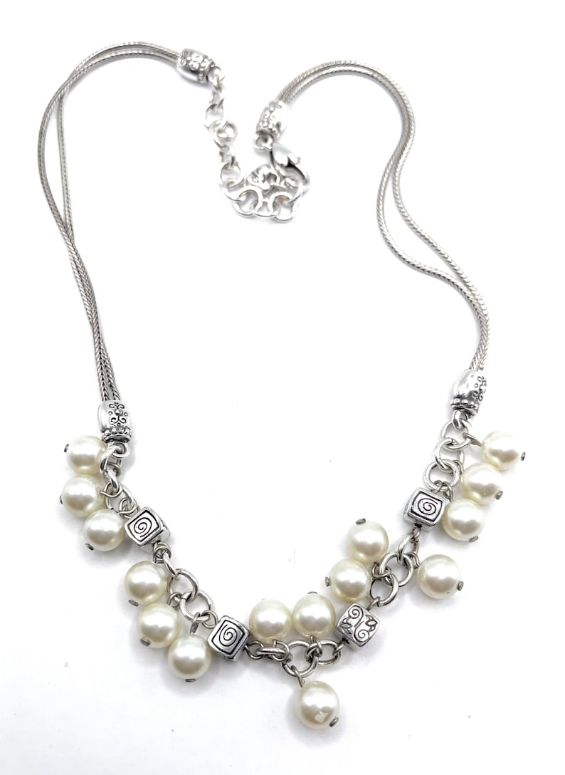 May include: Silver-toned necklace with multiple strands and a cluster of faux pearls. The necklace features decorative square links with a spiral design and a lobster clasp closure. The necklace is approximately 16 inches long.