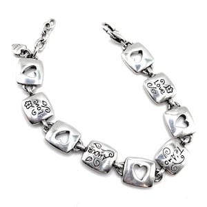 May include: Silver bracelet with square links, each with a heart-shaped cutout. The links are engraved with words such as "love" and "amour." It has a lobster clasp and a small heart charm.