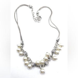 May include: Silver-toned necklace featuring a delicate chain and a cluster of faux pearls. The necklace has decorative square links with a swirl design. The necklace is a classic piece of jewelry.